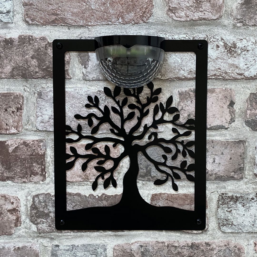 Open tree of life cut-out solar plaque on a pale brick wall