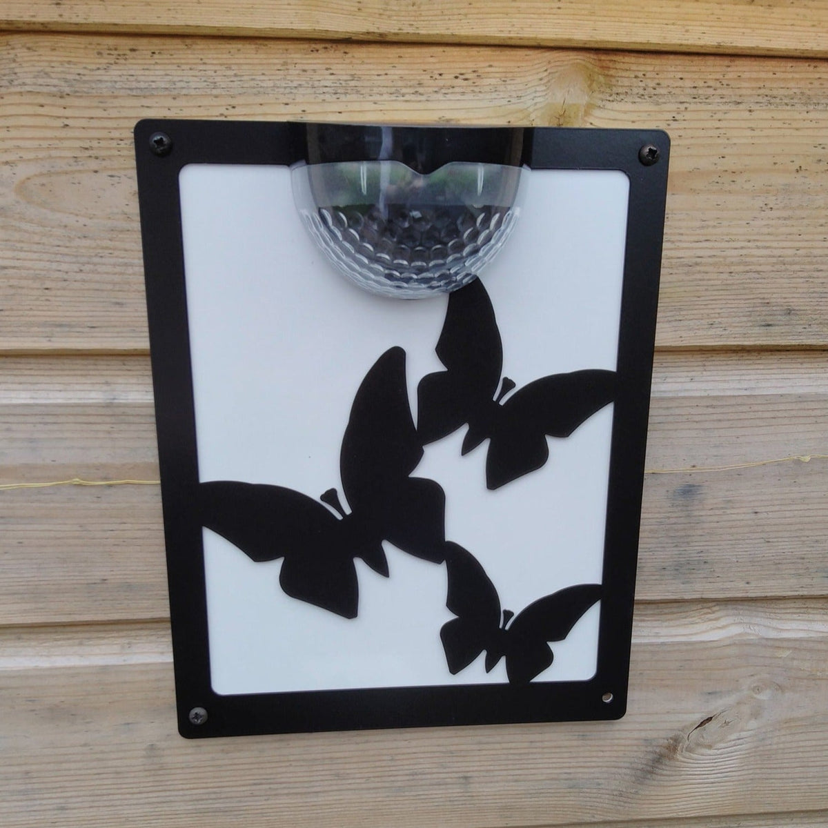 Butterfly solar plaque with white backing panel on a wooden fence
