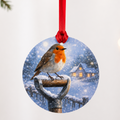 Round glass tree decoration with a robin on a garden spade handle and a snowy cottage, on a red ribbon