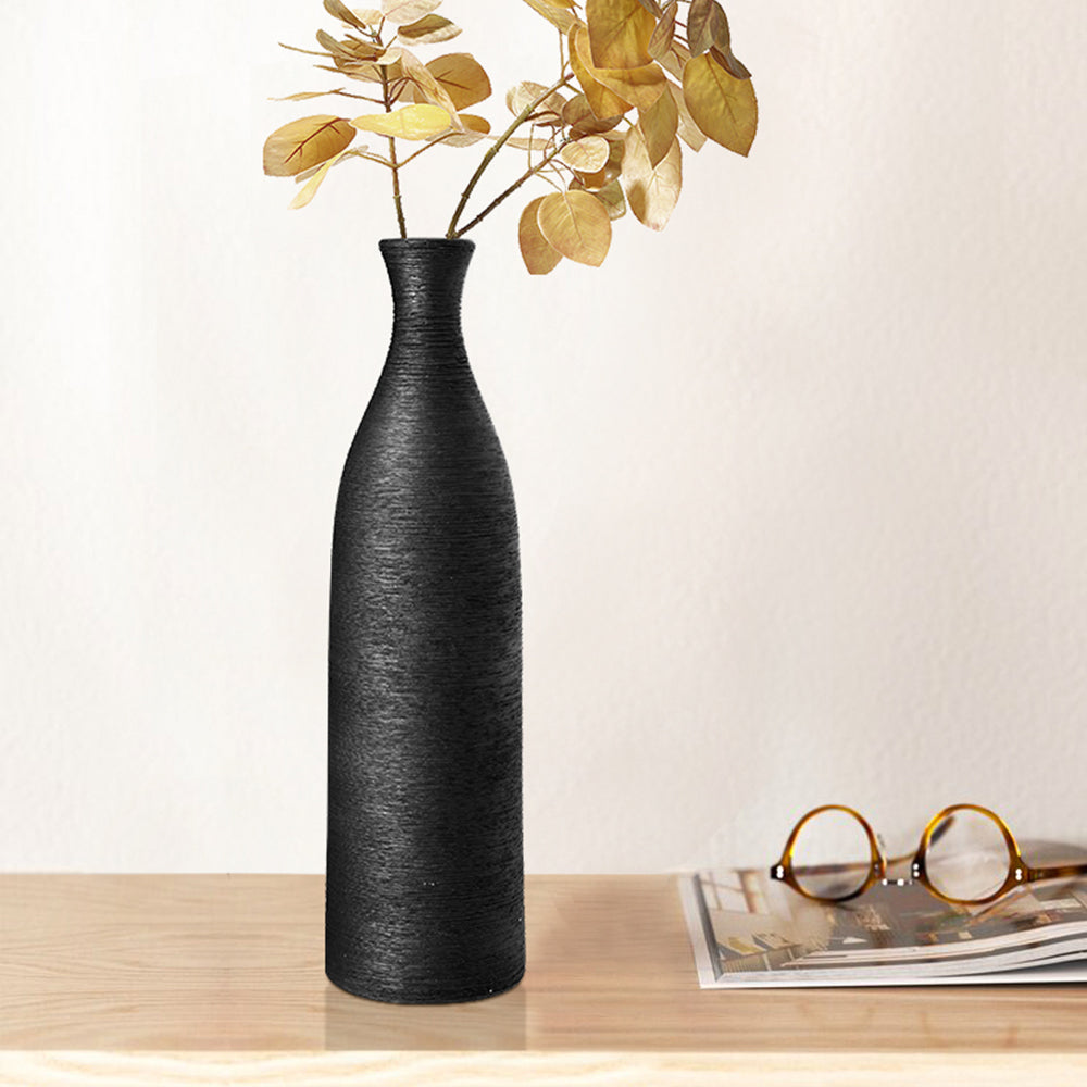 The black bottle vase with dried golden branches on a table beside books and glasses