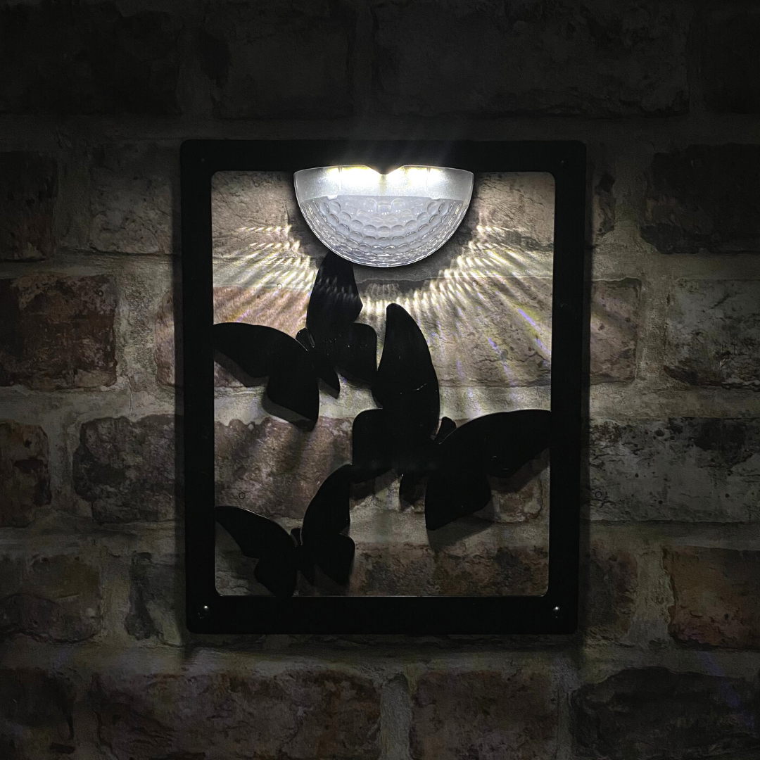 Open three-butterfly cut-out solar plaque lit at night on brick