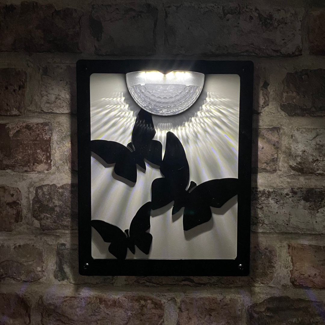 Butterfly solar plaque lit at night on a brick wall, light fanning down over three butterflies