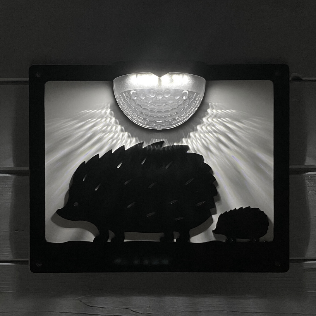 Hedgehog solar wall plaque at night, its domed lamp shining white light down over the cut-out