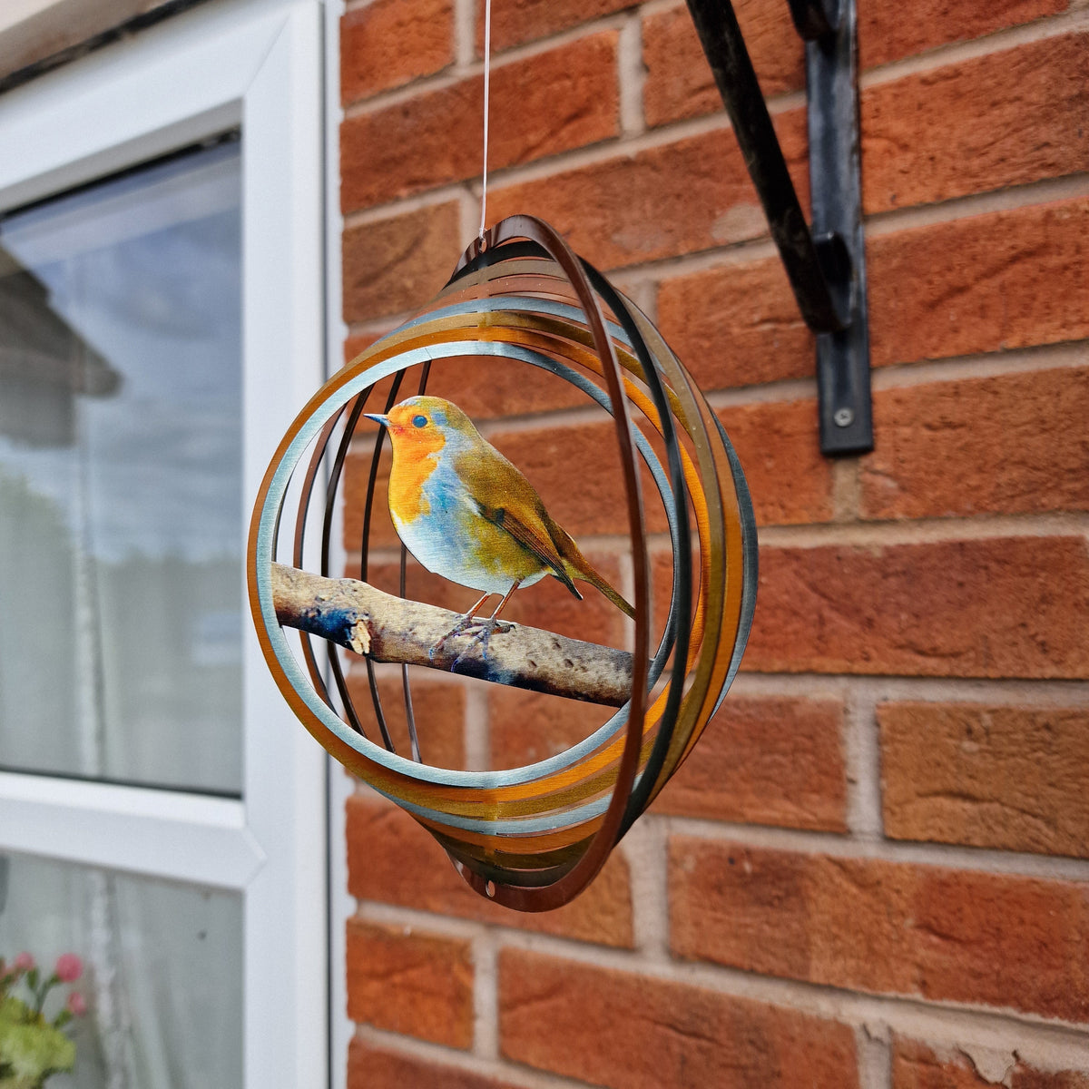 Robin wind spinner turning on a black wall bracket beside a brick house