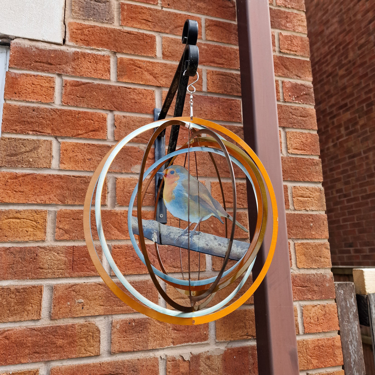 Robin wind spinner hanging from a black bracket on a brick wall