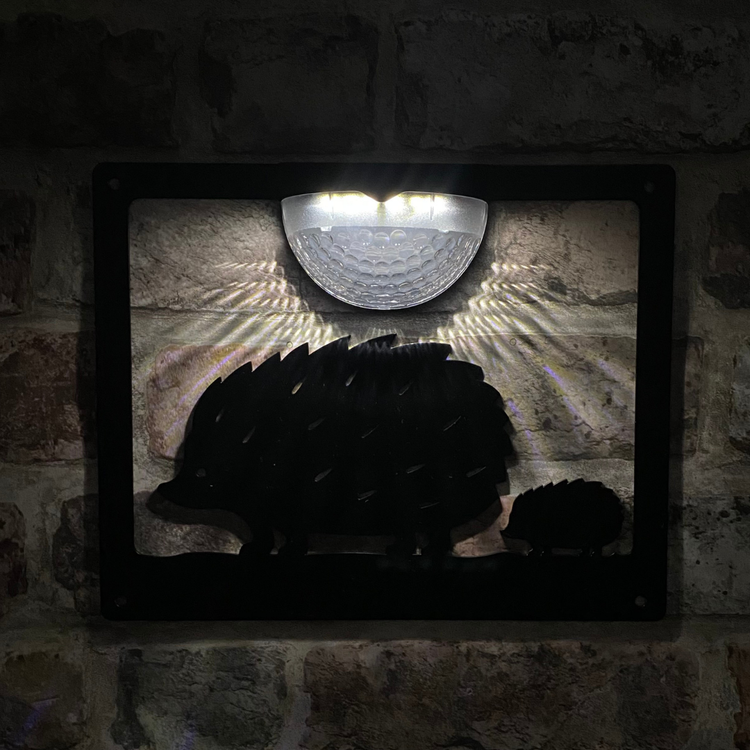 Open hedgehog cut-out solar plaque lit at night on a brick wall