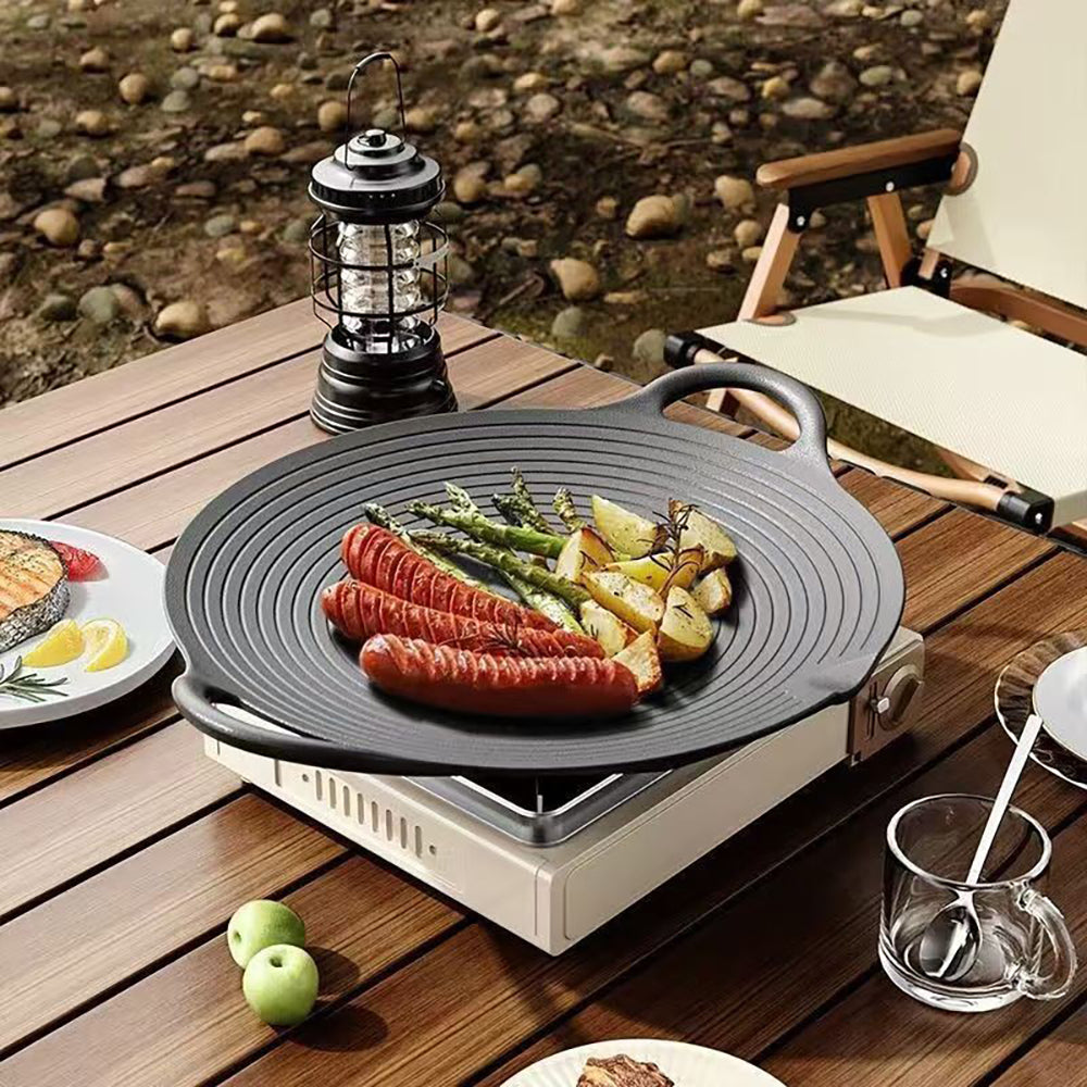 Cast iron grill pan with sausages and asparagus on a camping stove on a wooden table