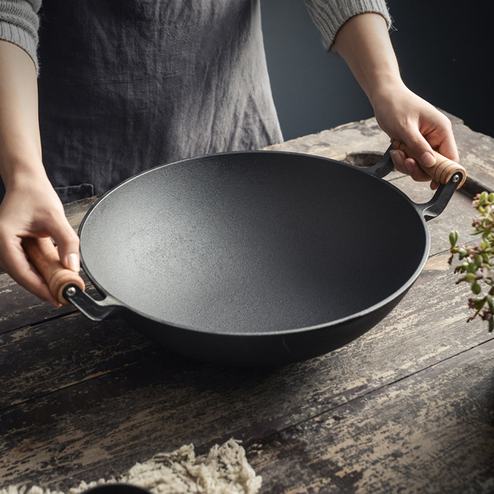 Two hands holding the empty cast iron wok by its wooden handles over a wooden table