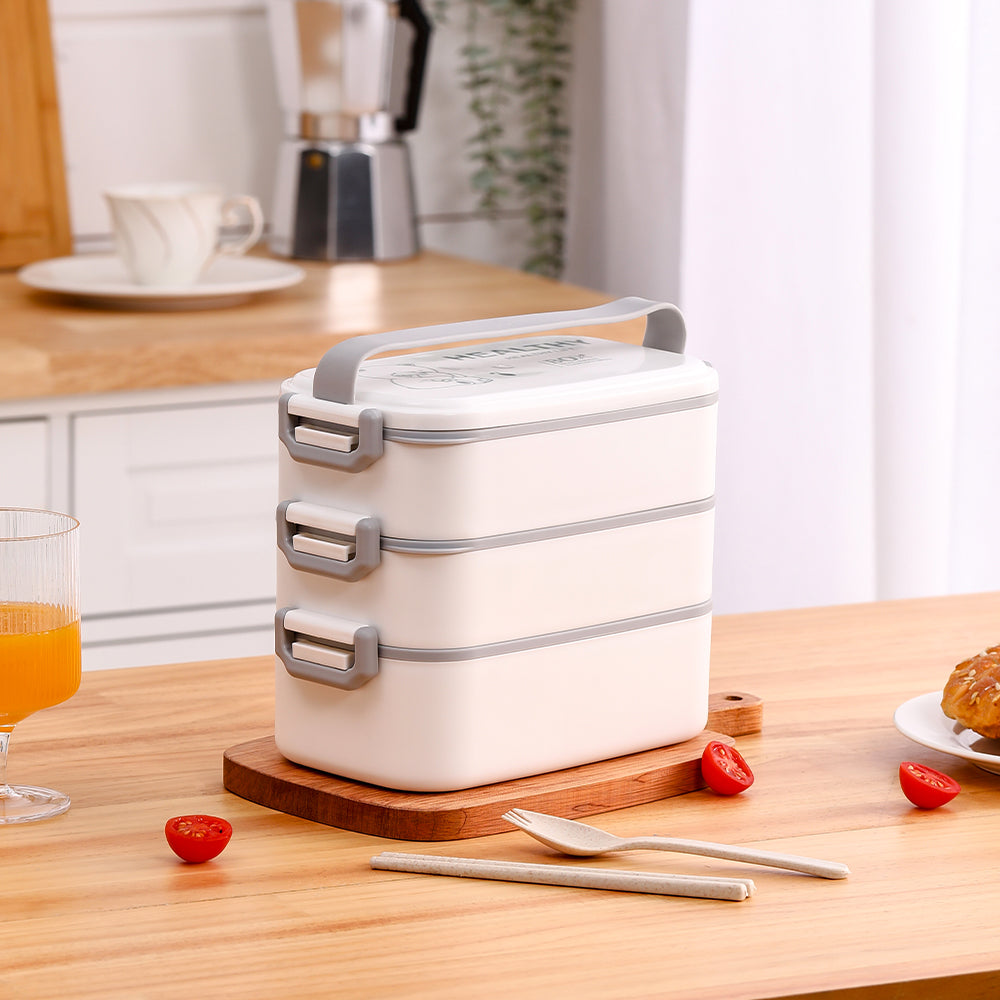 White three-tier lunch box with grey clips and a grey carry handle on a wooden board in a kitchen