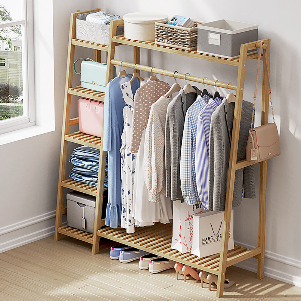 The bamboo clothes rack in a bedroom holding coats, shirts, bags and shoes