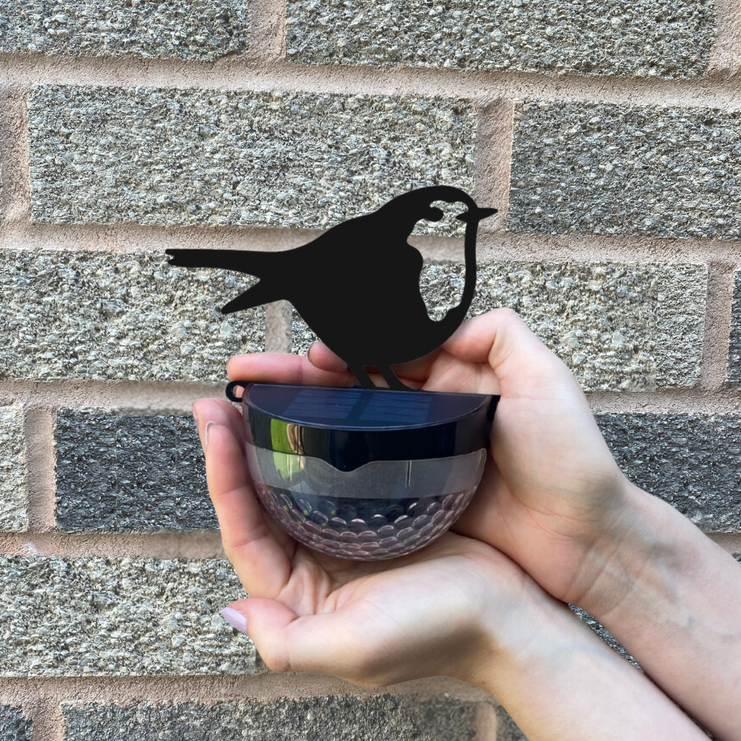 A hand holding the robin solar light in front of a brick wall