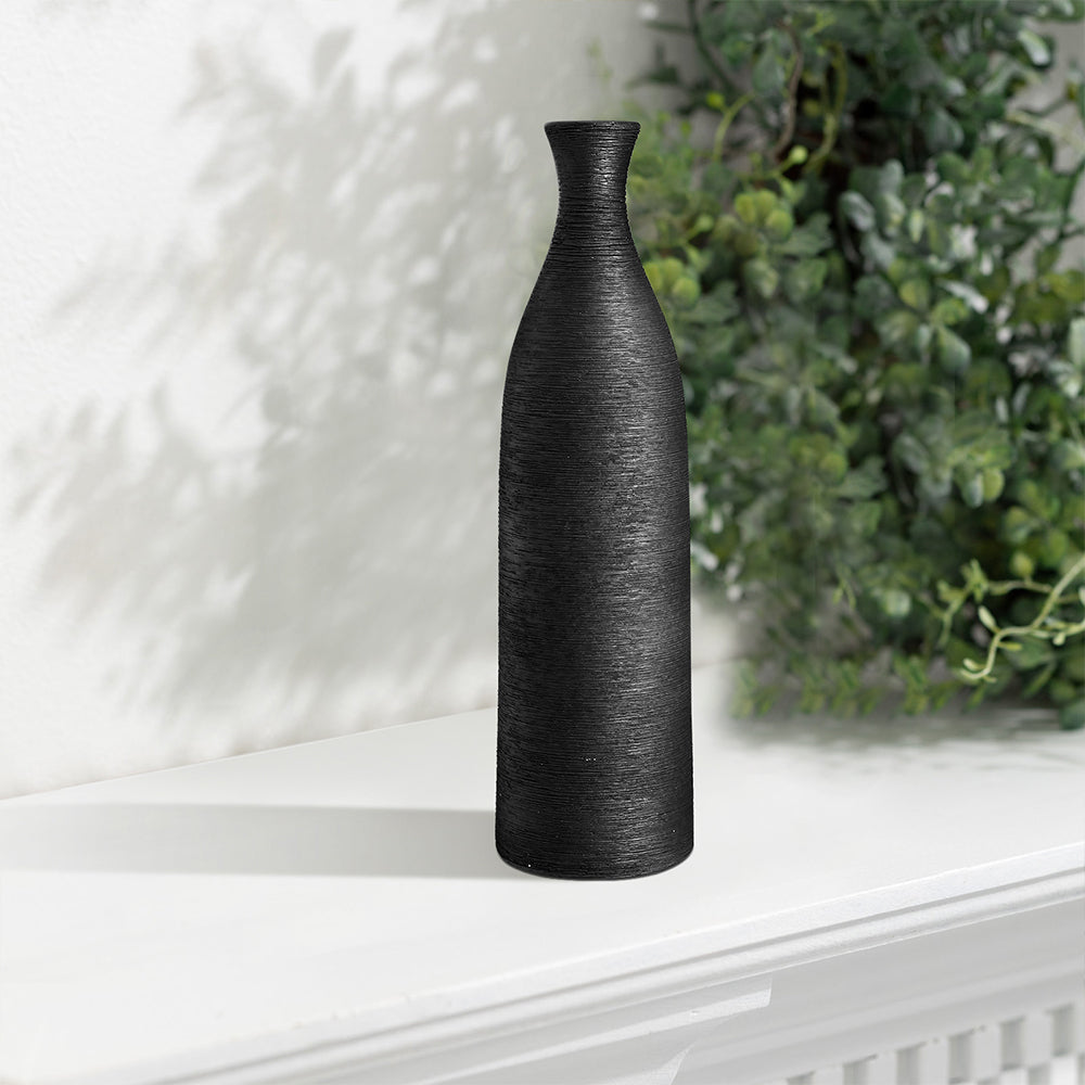 The tall black bottle vase on a white shelf beside green plants