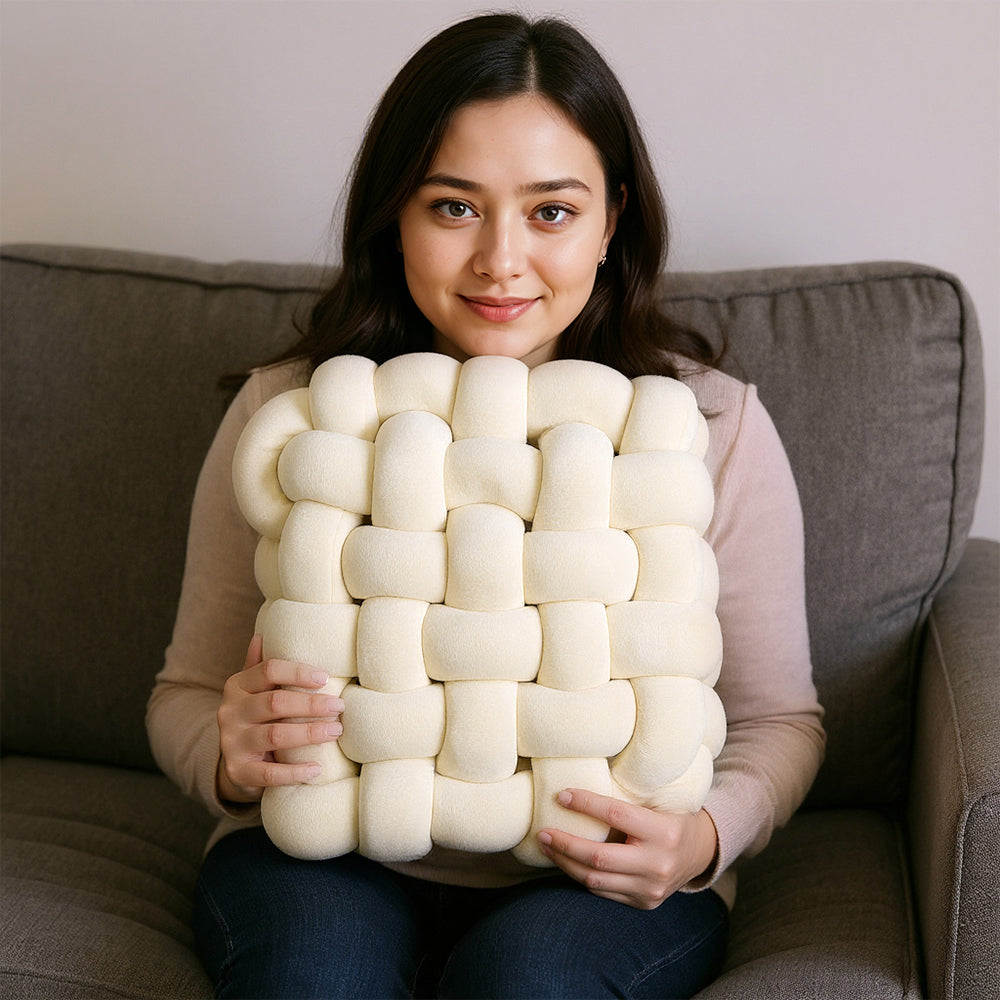 Woman on a grey sofa holding the cream knotted seat cushion in front of her