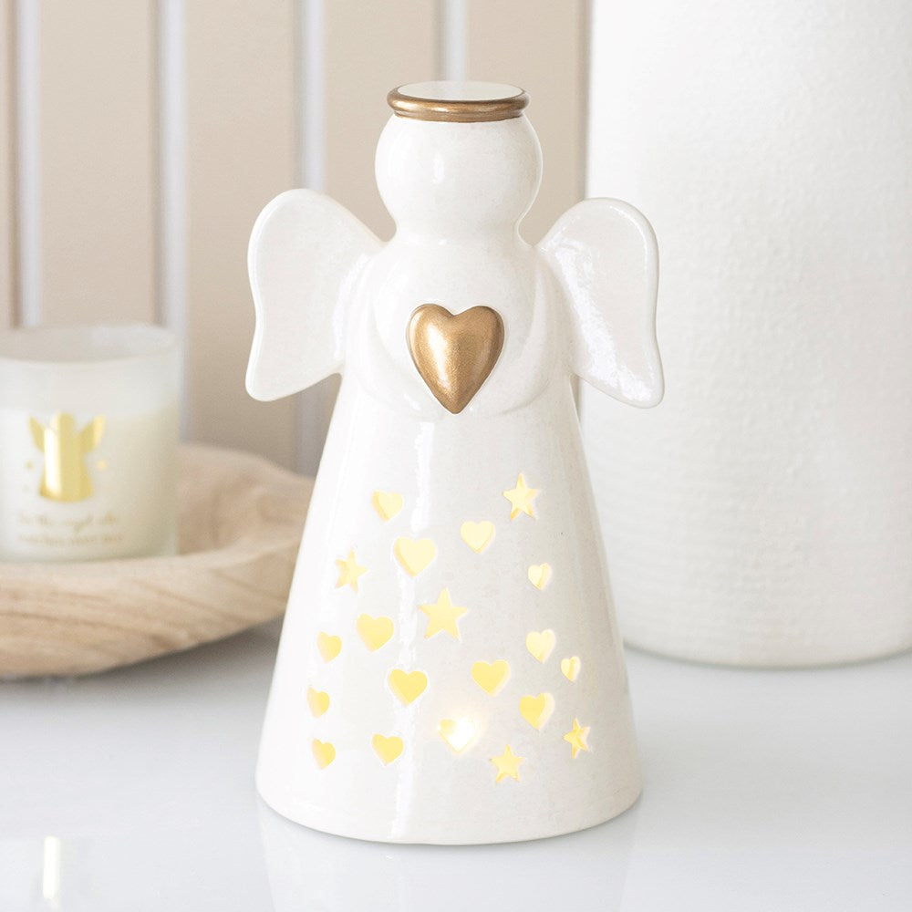 Off-white ceramic angel holding a gold heart, lit from inside through heart and star cut-outs
