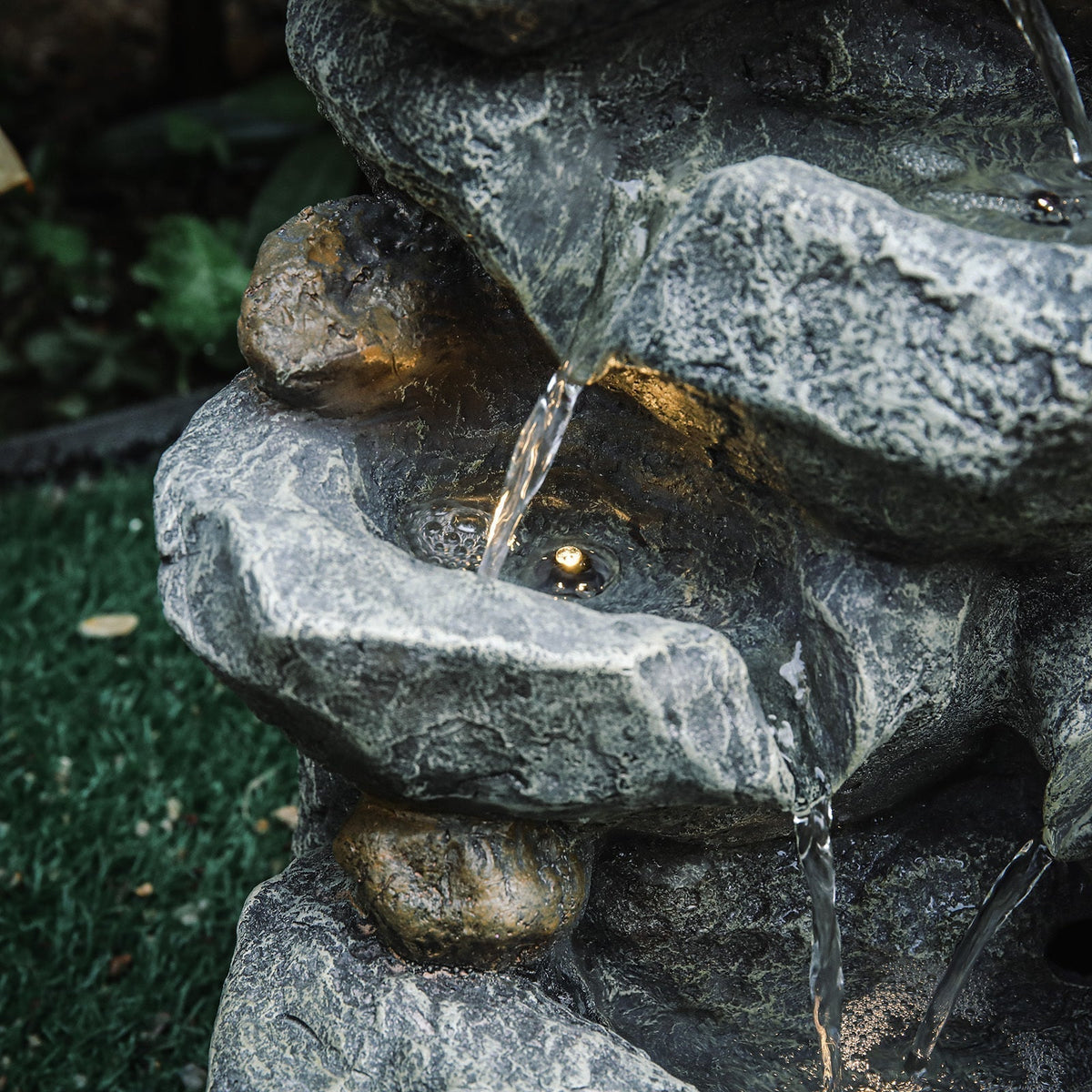 Close-up of water pouring from a rock ledge into a bowl lit by a small LED