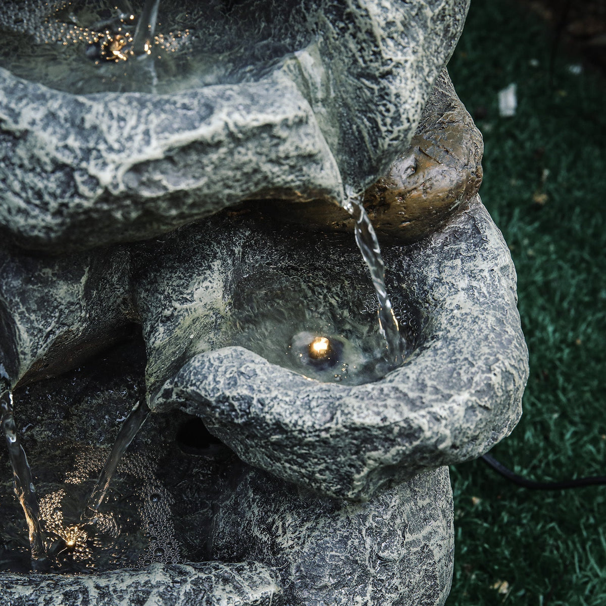 Close-up of a rock bowl with a glowing LED and water falling past a pebble