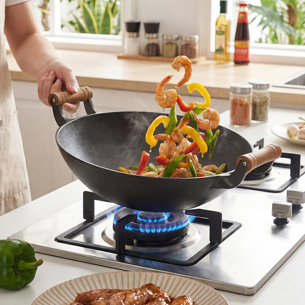 Cast iron wok tossing prawns and peppers over a gas flame, held by one wooden handle