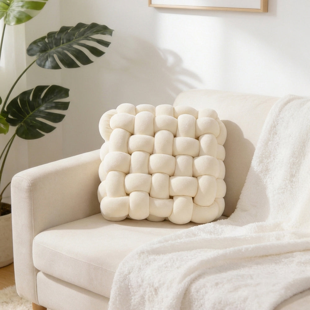 Cream knotted cushion standing against the back of a white armchair