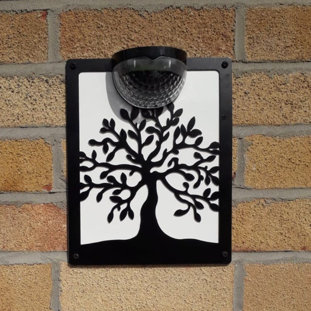 Tree of life solar plaque with white backing panel on a brick wall