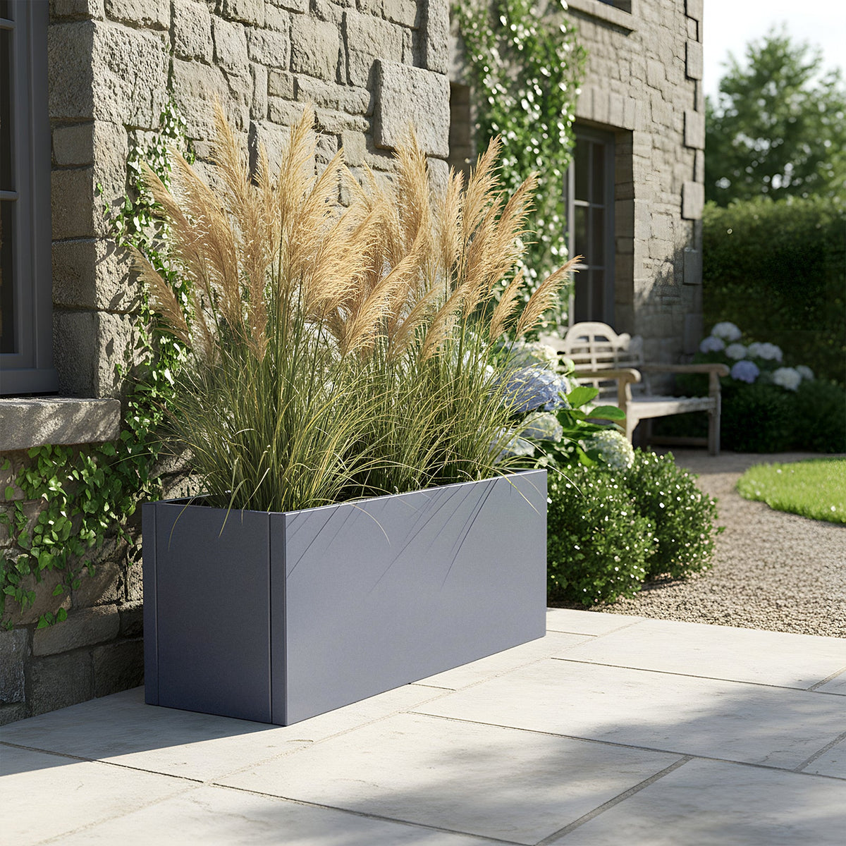 Dark grey rectangular metal planter with tall ornamental grass on a stone patio