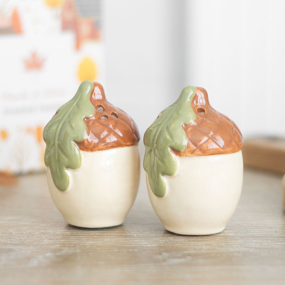 Two ceramic acorn shakers with russet caps and green oak leaves on a light wooden table