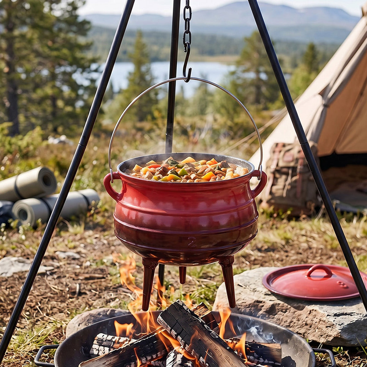 Red enamelled cast iron cauldron of stew hanging from a tripod over a campfire, its lid on a rock