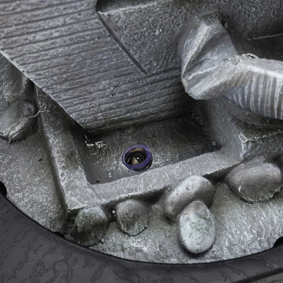 Close-up of the pump outlet and grey resin pebbles at the fountain base
