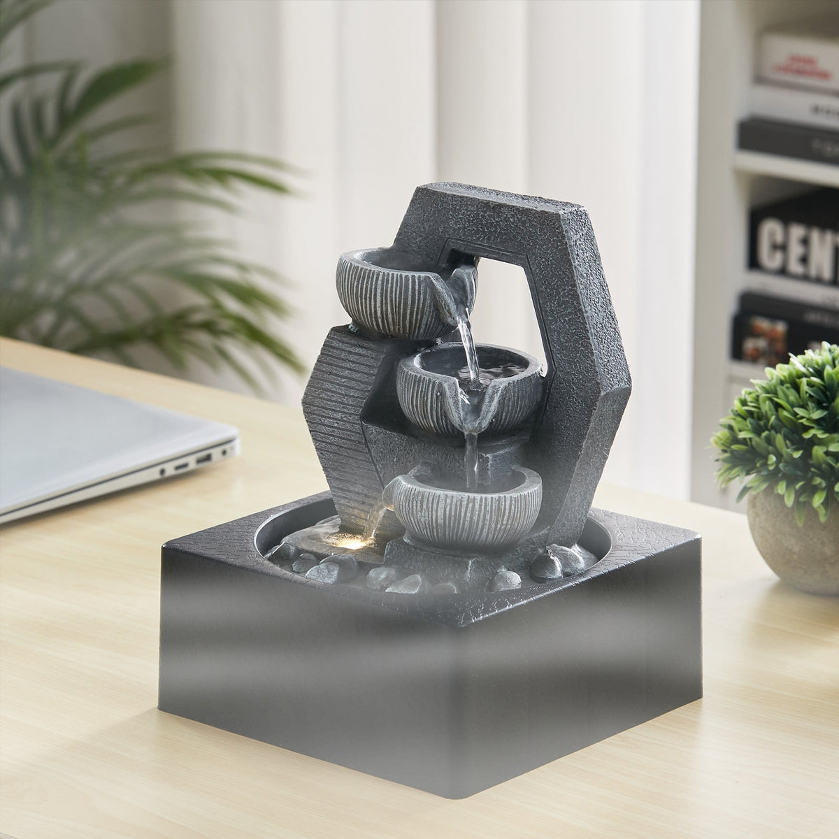 Grey cascade tabletop fountain on a wooden desk beside a small plant