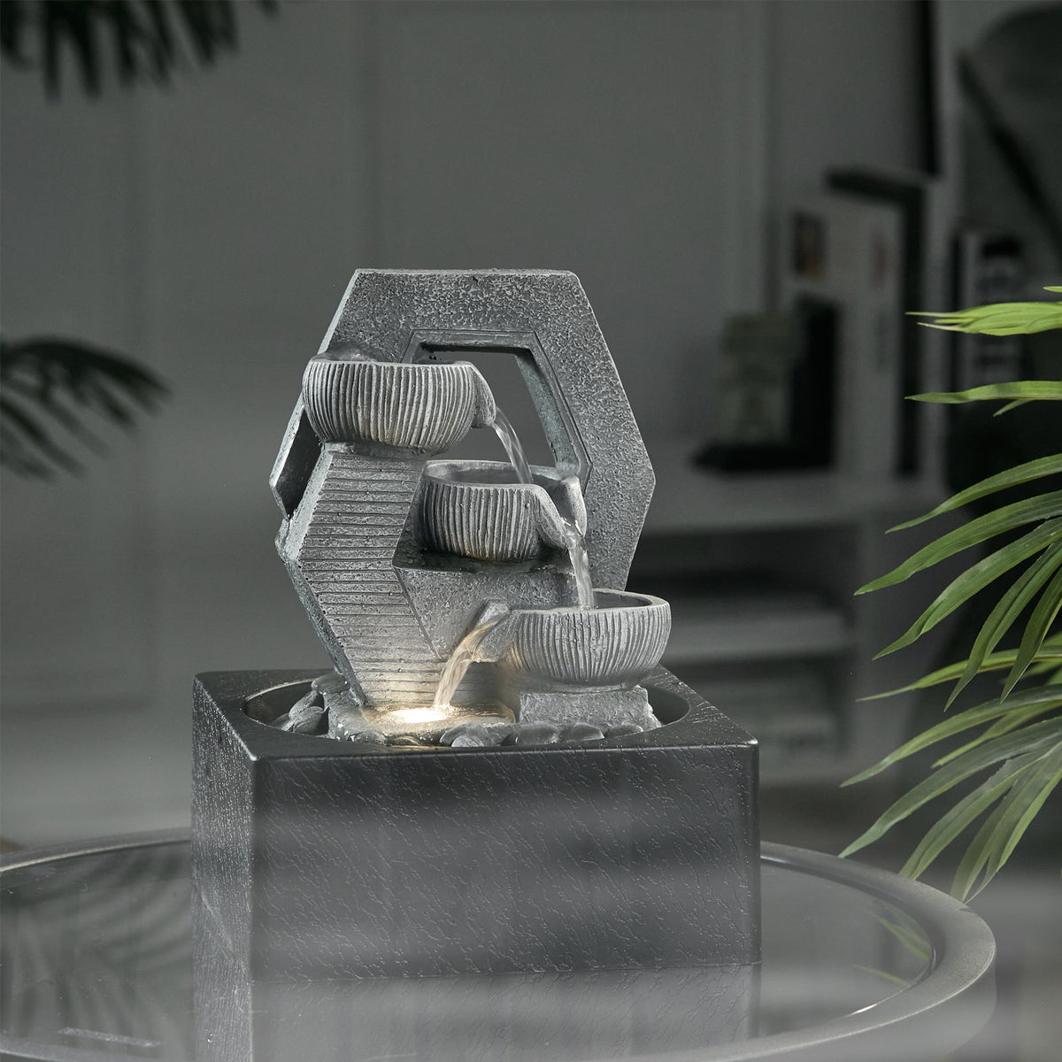 Grey hexagonal tabletop fountain on a glass table in a dim room