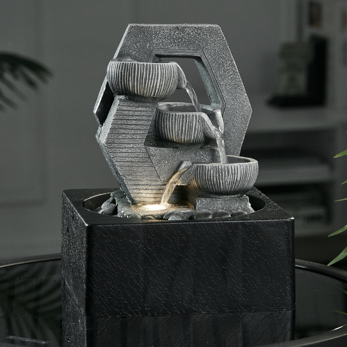 Cascade fountain with water falling through three bowls, LED lit, on a dark table