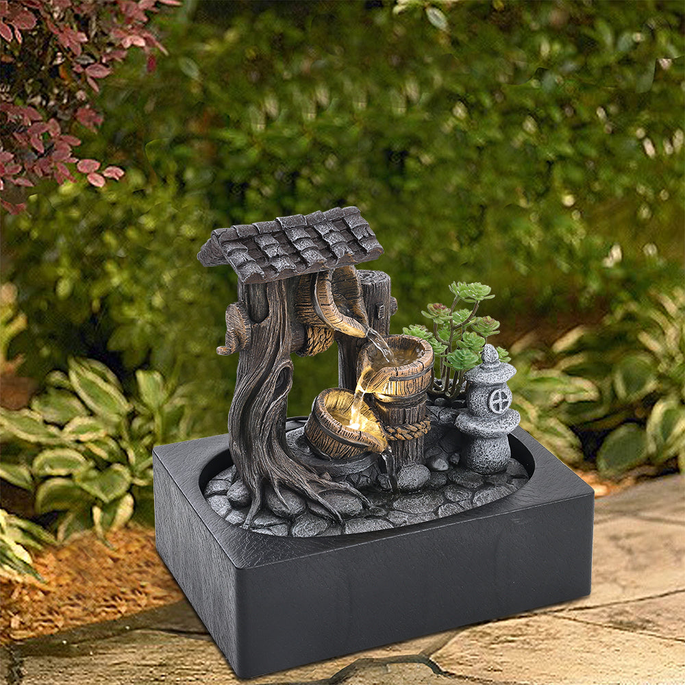 Tabletop fountain with its tree, roof and buckets set among garden plants