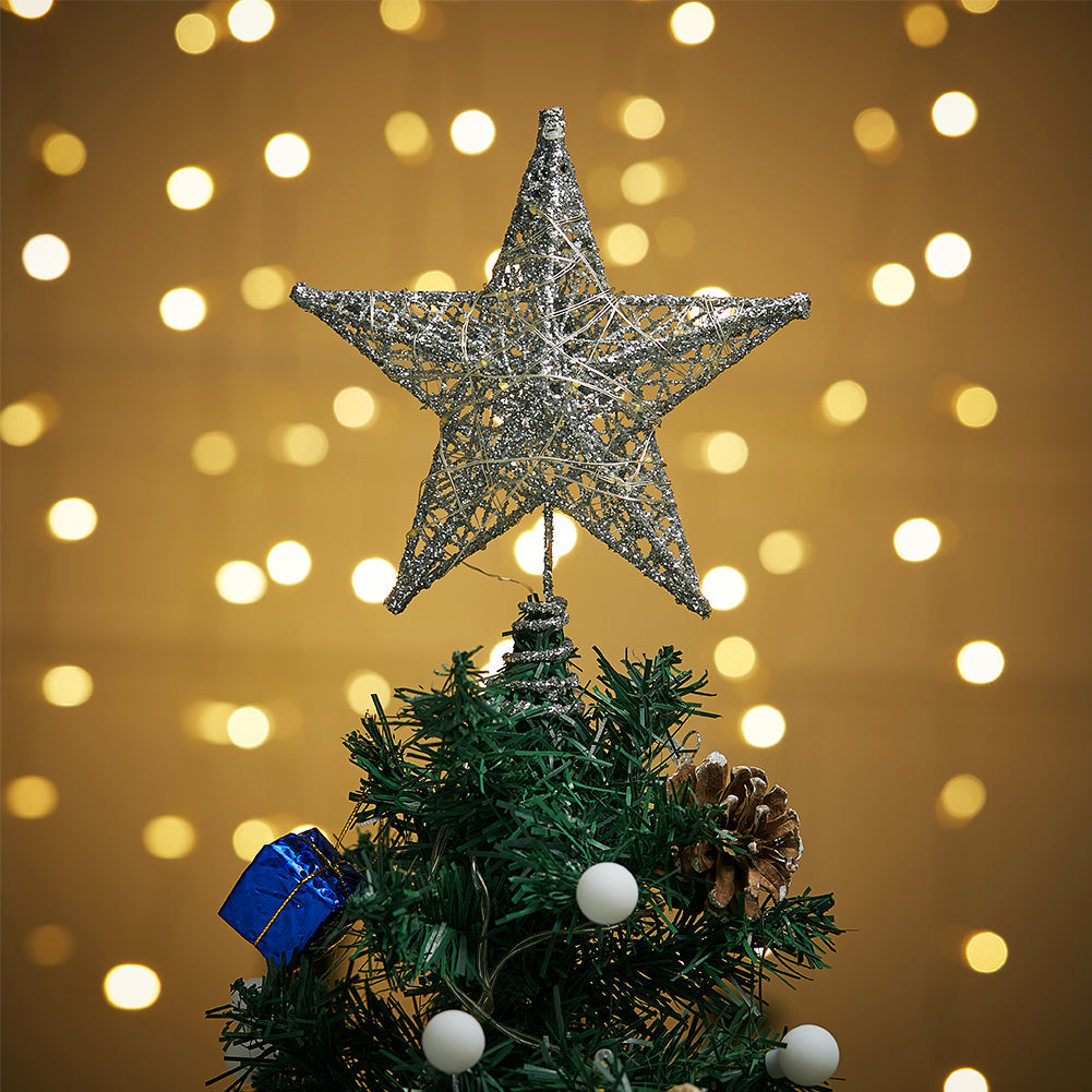 Silver glittered star topper on top of a small tree against warm bokeh lights