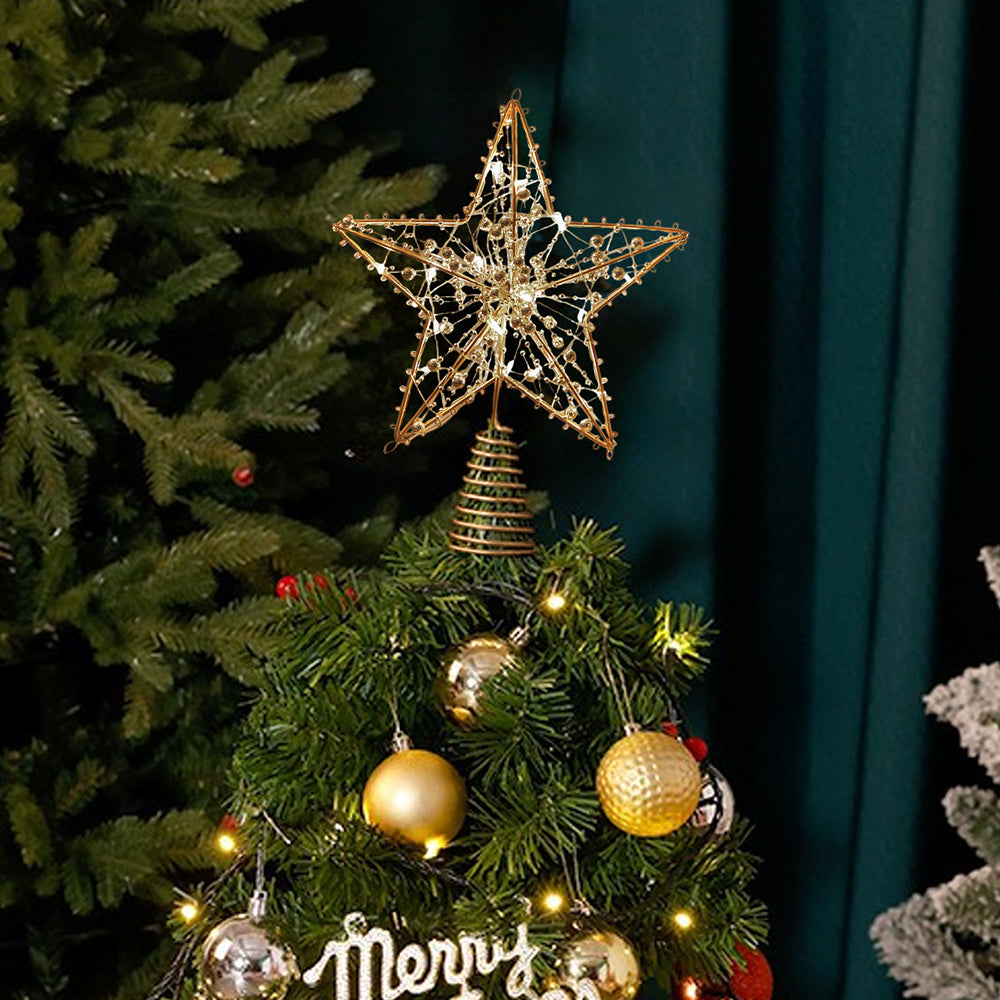 Gold wire star topper on a decorated Christmas tree with gold baubles by a green curtain