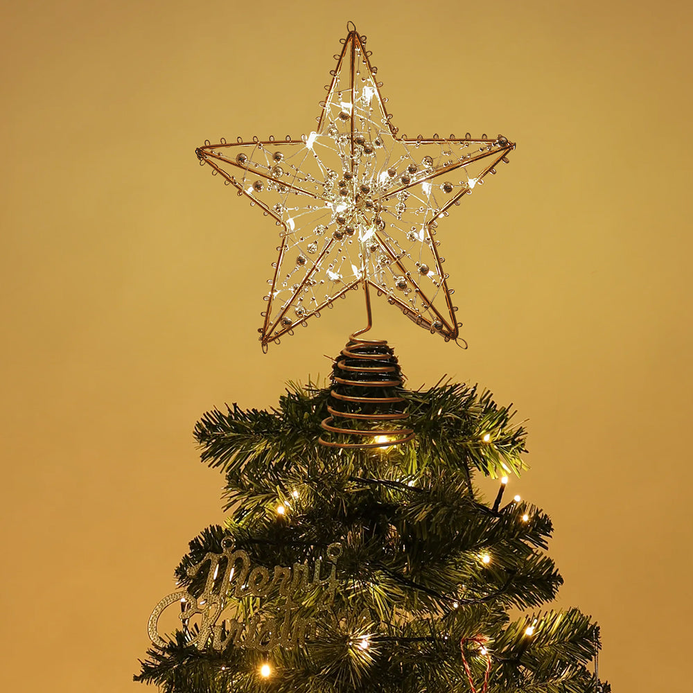 Lit gold wire star topper with beads on top of a Christmas tree against a warm wall