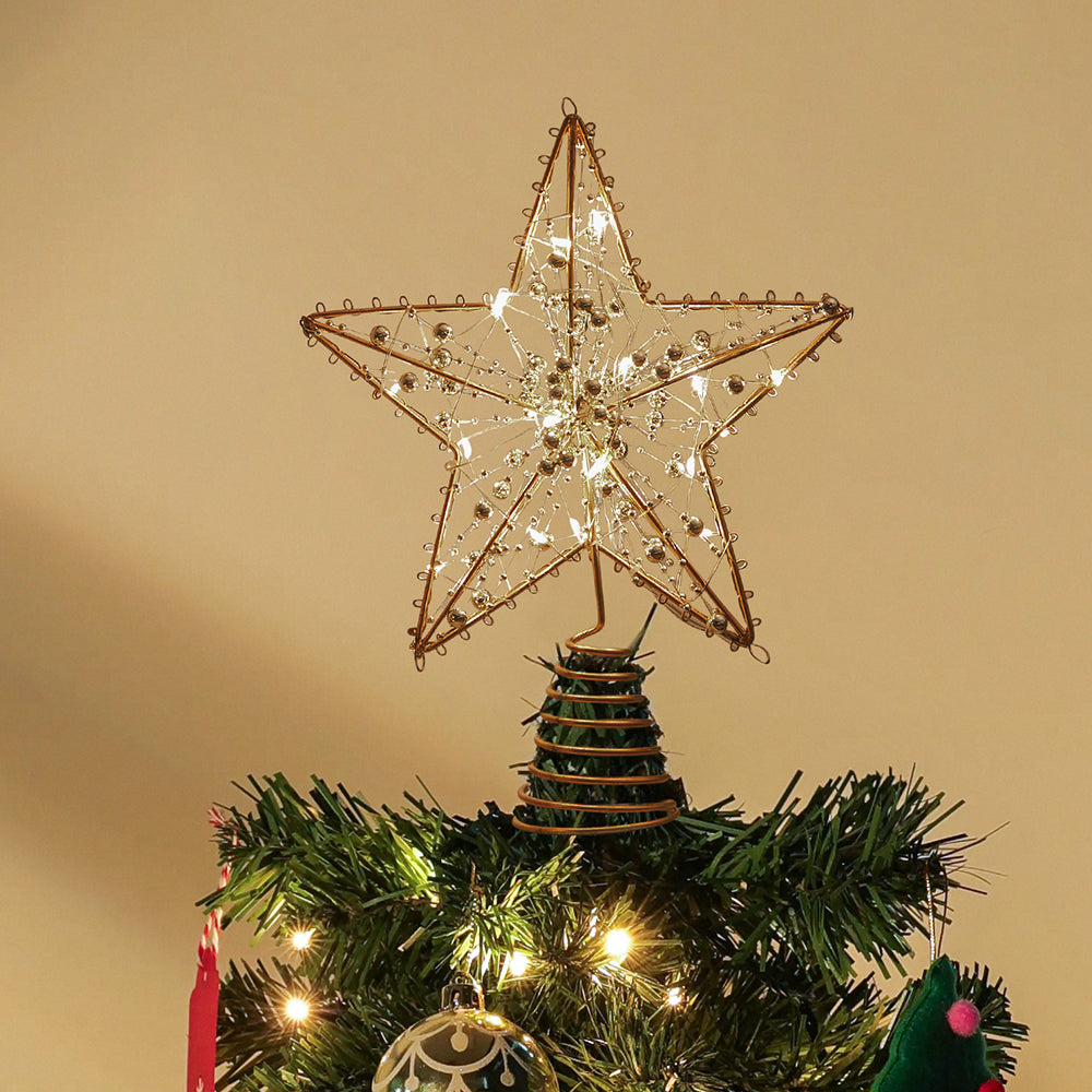 Gold beaded wire star topper on its spiral base on top of a lit Christmas tree