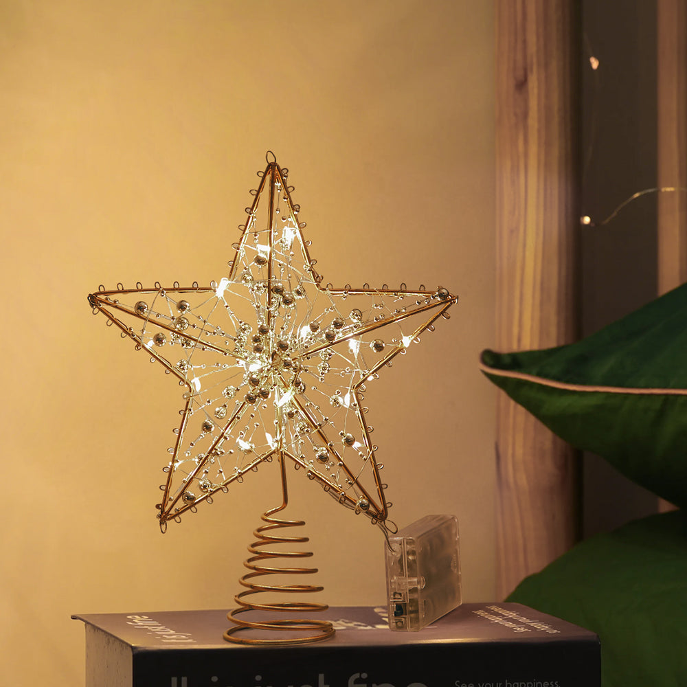 Lit gold beaded star topper standing on its spiral base on a stack of books