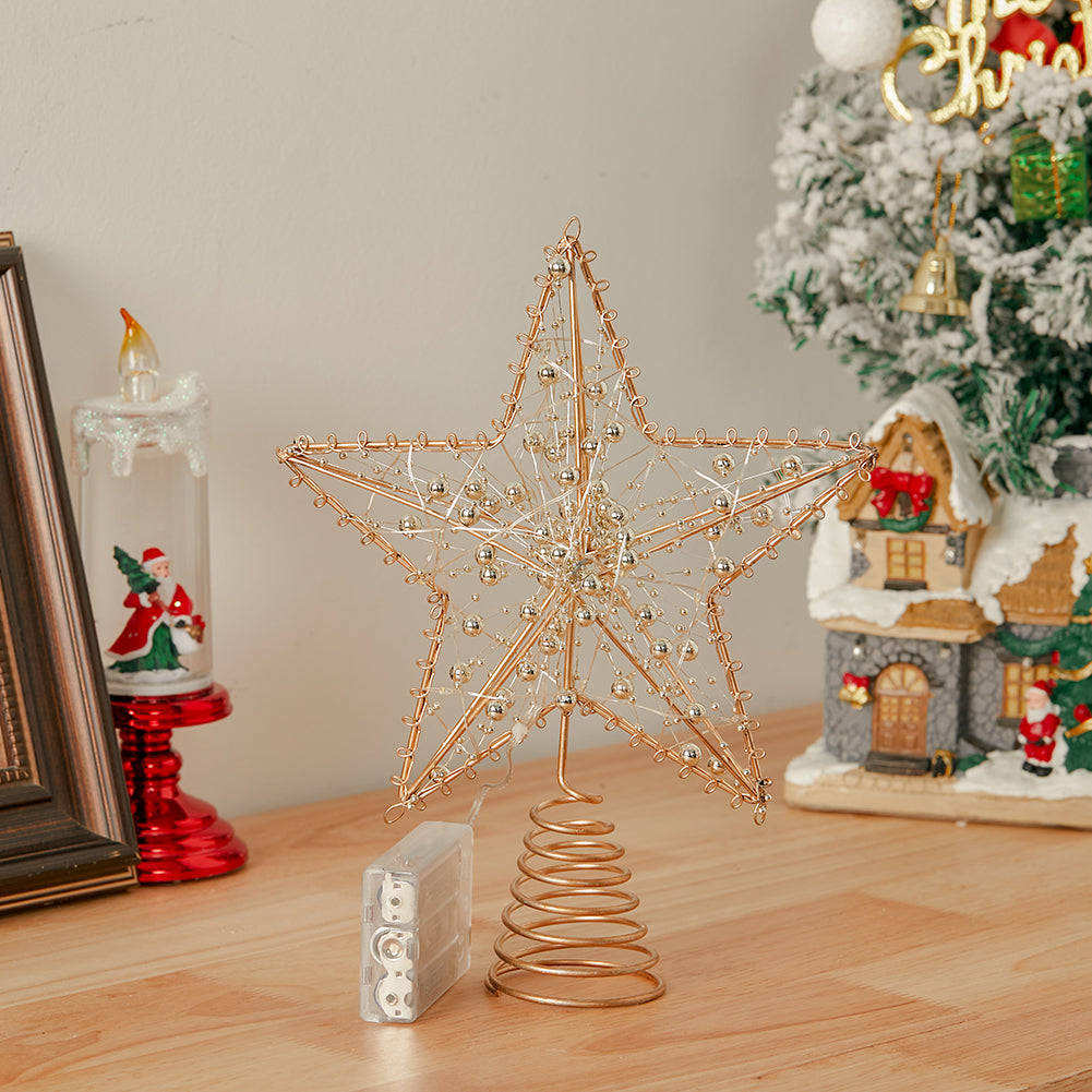 Unlit gold wire star topper with beads standing on a wooden table beside its battery box