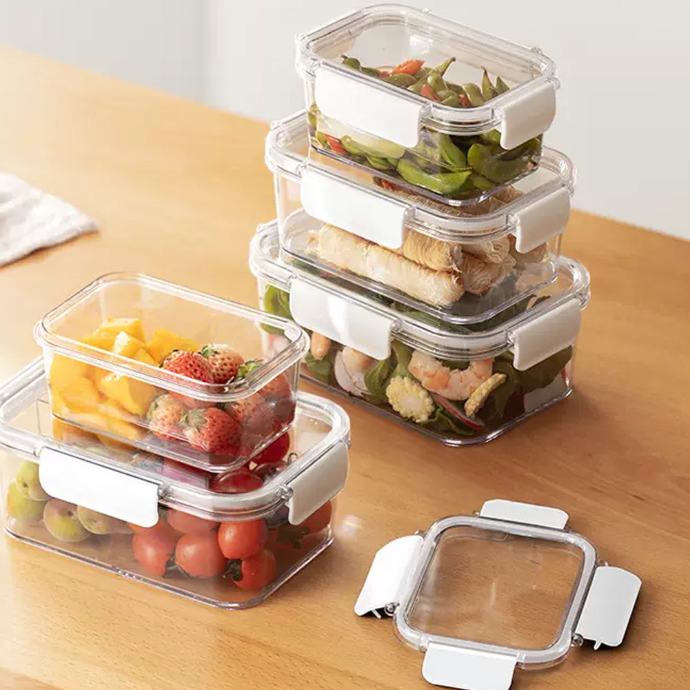 Clear clip-lid boxes stacked with salad, noodles and fruit on a wooden worktop, one lid beside them