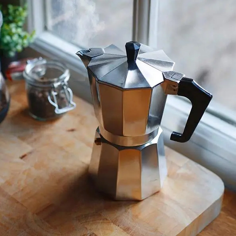 Eight-sided moka pot on a wooden board by a window with a jar of coffee