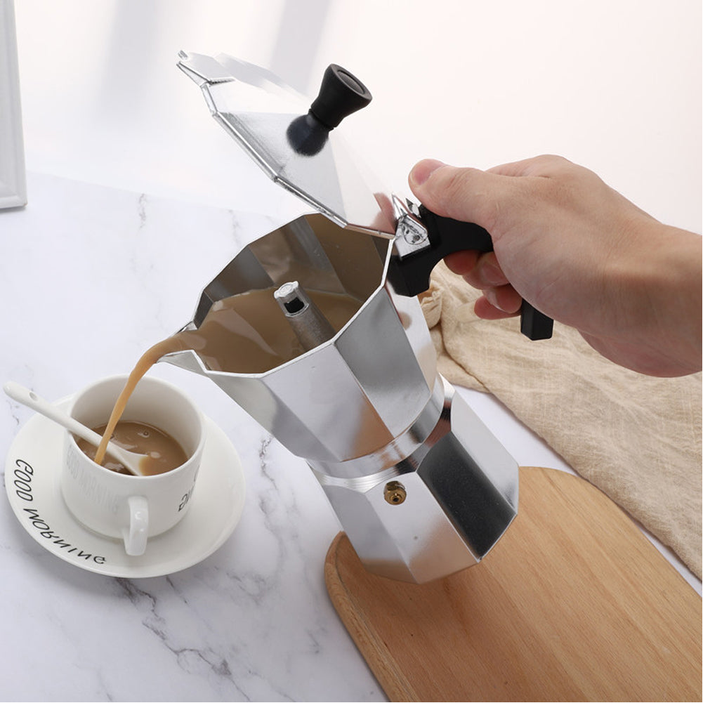 Hand pouring milky coffee from the aluminium moka pot into a cup on a saucer