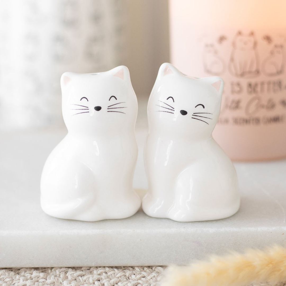 Two white ceramic cat salt and pepper shakers side by side on a marble shelf
