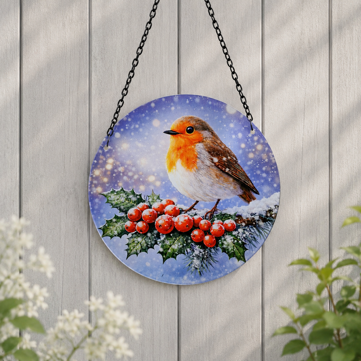 Glass robin suncatcher hanging on a grey wooden fence above white flowers
