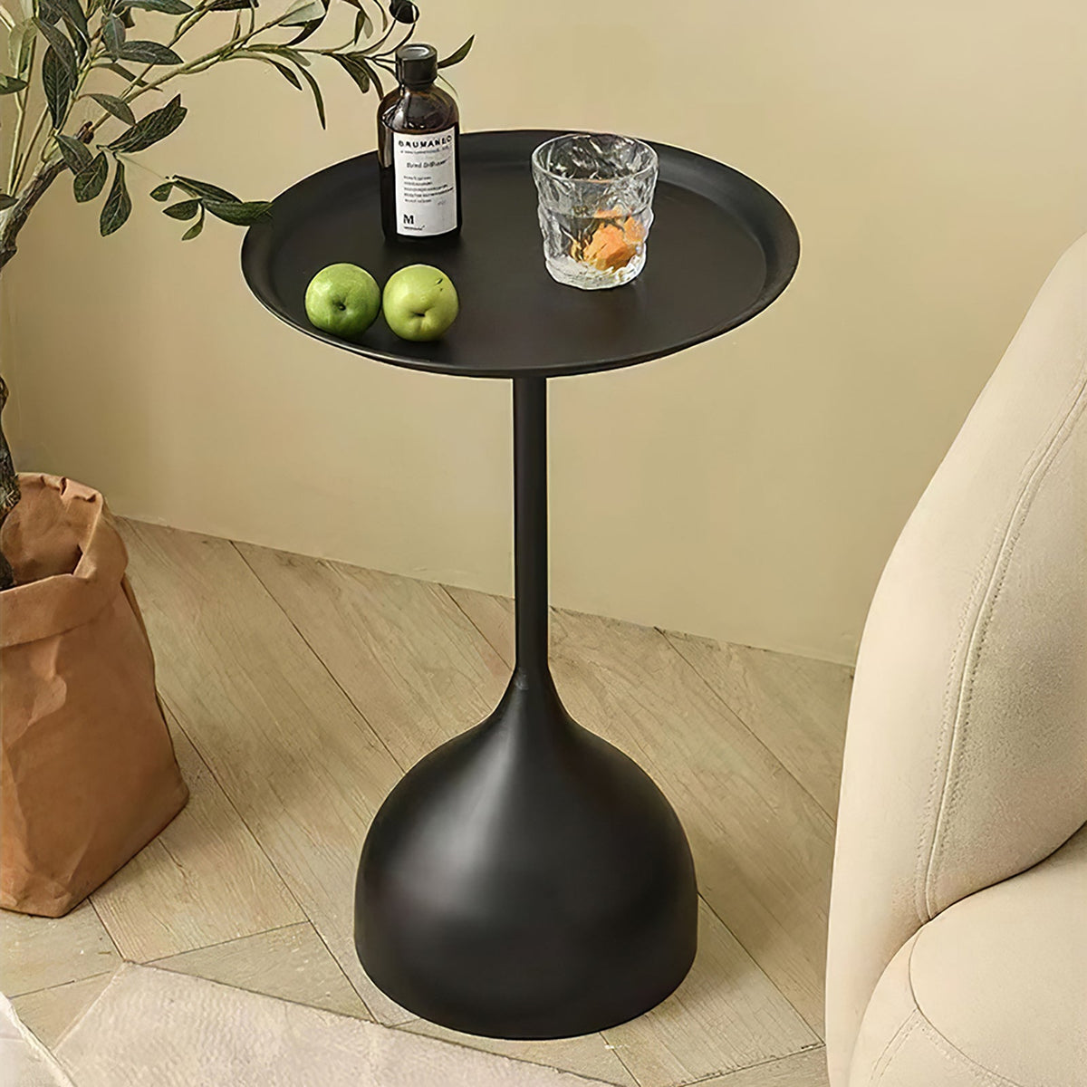 Black round side table holding green apples and a glass beside an armchair