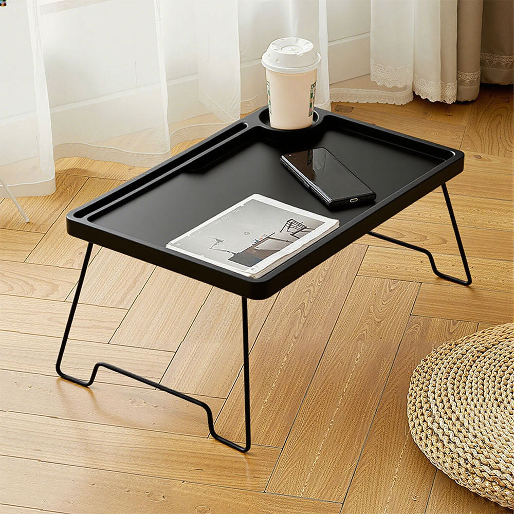 Black folding bed table on a bed holding a book and a drink