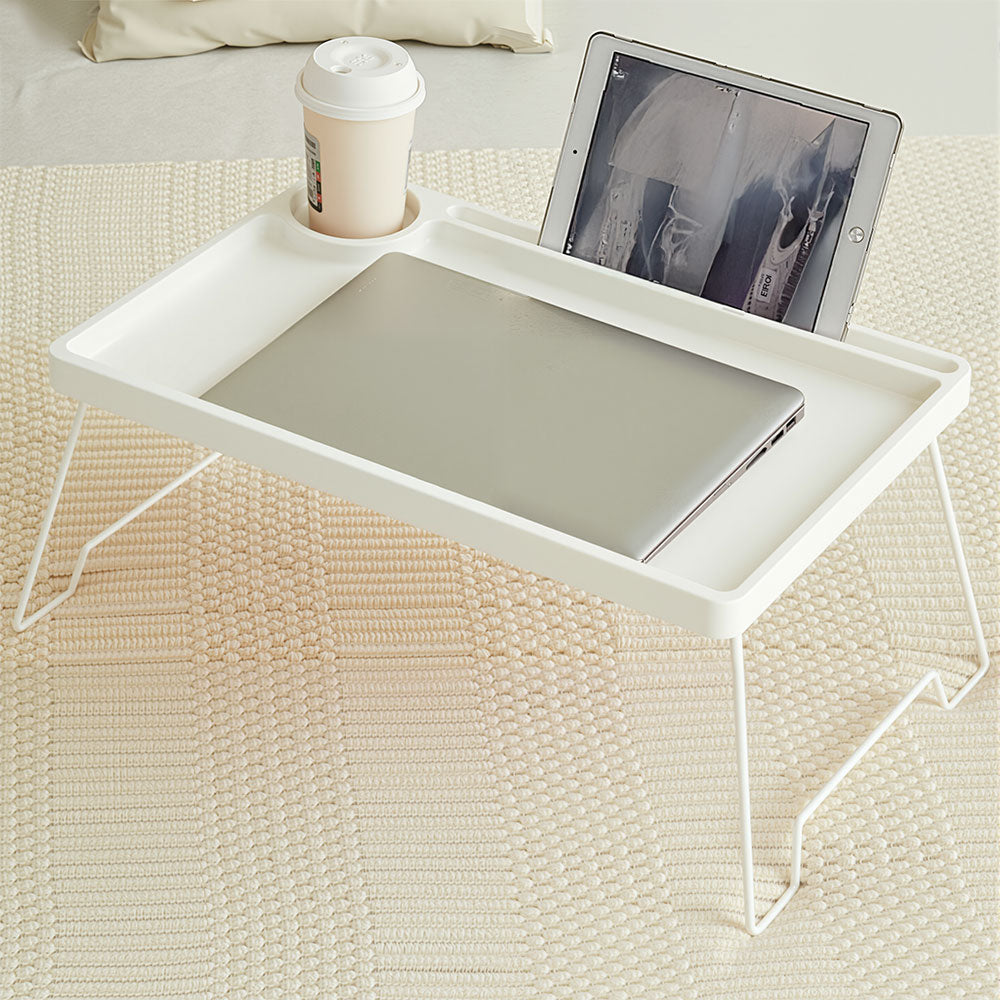 White folding bed table holding a laptop, a tablet and a cup on a bed