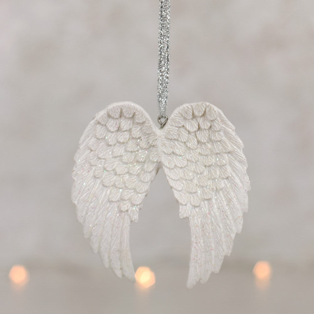 The white glitter angel wings hanging on a silver ribbon in soft light