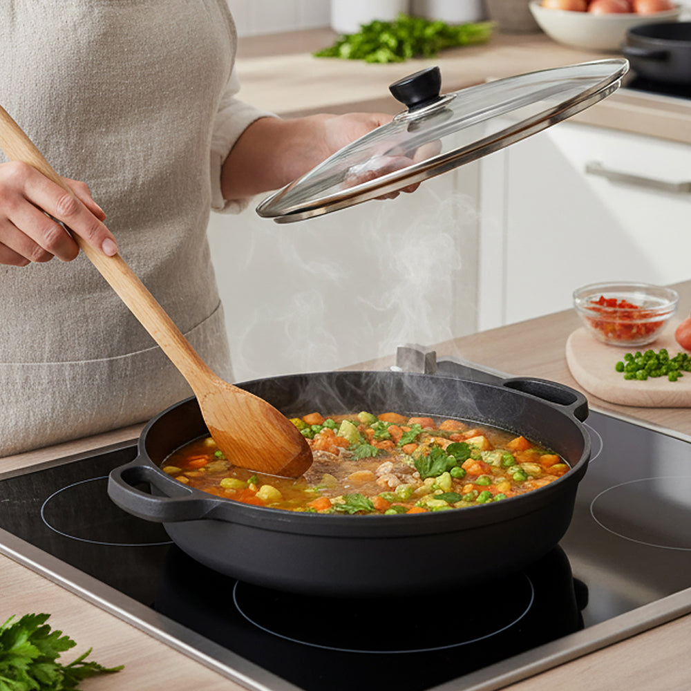 A cook lifting the glass lid off a steaming stew in the braiser on an induction hob