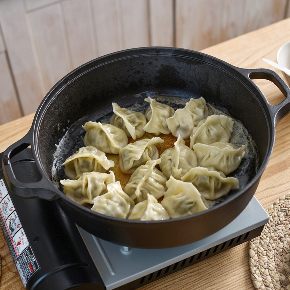 Dumplings frying in the cast iron braiser on a portable gas stove