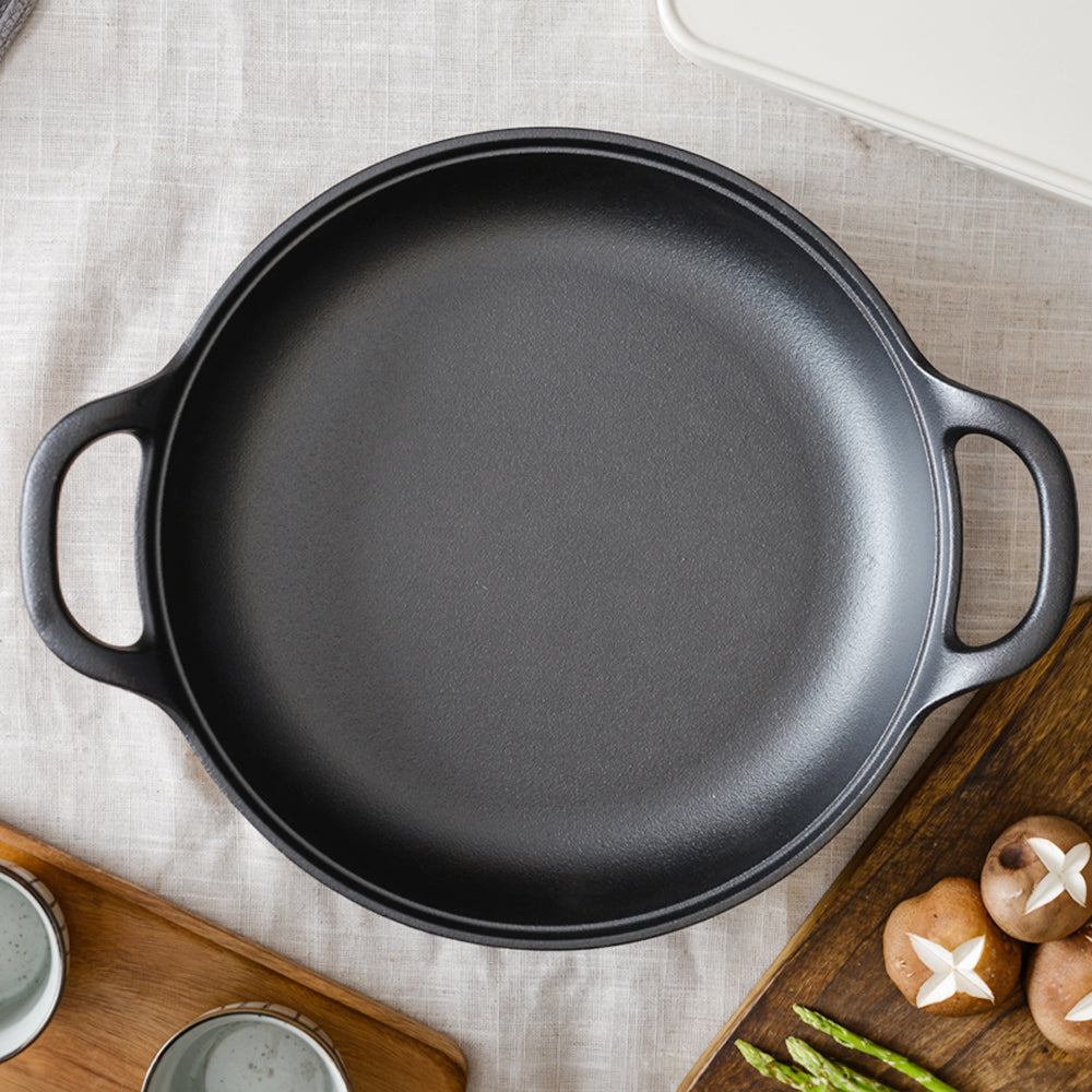 Top view of the empty cast iron braiser with two loop handles on a linen cloth