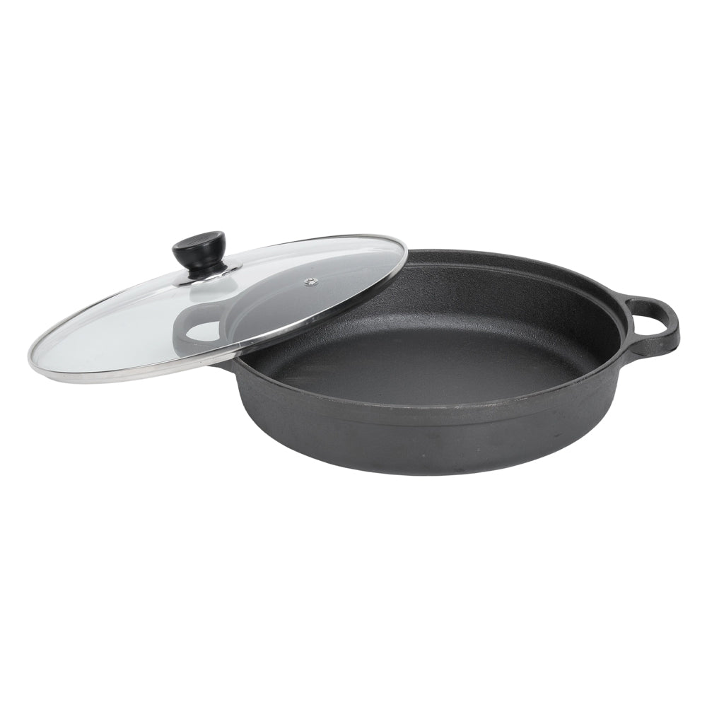 Black cast iron braiser with two loop handles and its glass lid with a black knob beside it, on white